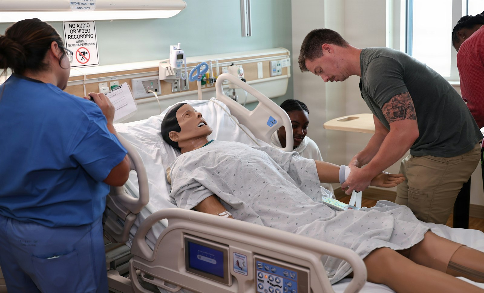 Nursing students practicing a simulated emergency scenario around a bedside monitor